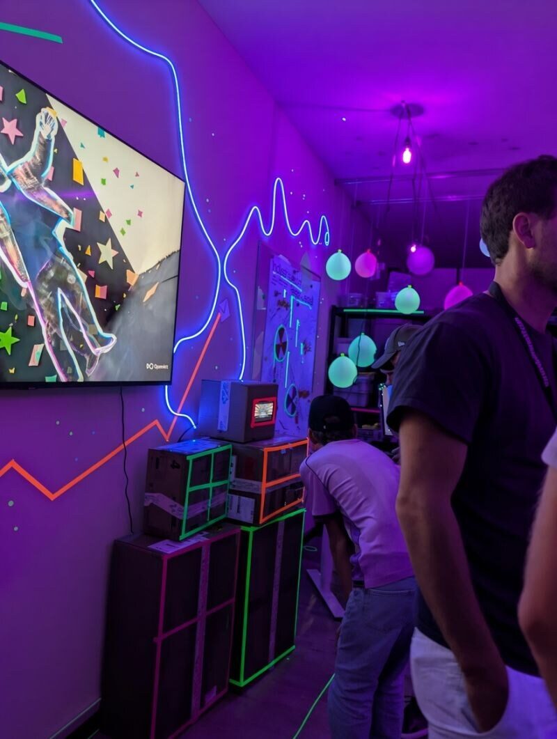 Foto: Büro im violetten UV-Licht mit Grossbildschirm und einem Röhrenfernseher auf neonbeklebten Kisten
